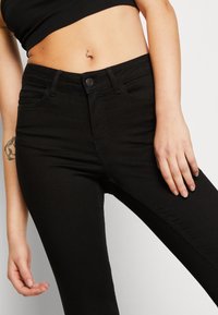 Vaqueros de denim negro con un diseño ajustado, estilo de cinco bolsillos, cierre frontal con botón y detalles de costura sutiles. Textura suave, acentos mínimos.