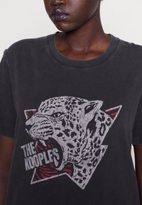 Černé bavlněné tričko s grafikou leopardu se strukturovanými detaily, červenými a šedými akcenty a kulatým výstřihem. Součástí je logo značky.