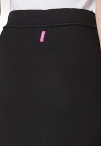 Schwarzer knielanger Rock aus elastischem Material, mit einem pinken DEHA-Tag. Glatte Textur mit einem taillierten Bund.
