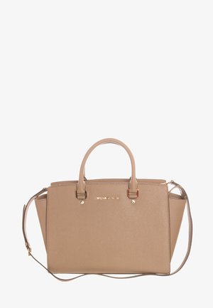 Beżowa skórzana torebka Michael Kors z górnymi uchwytami i regulowanym paskiem na ramię, z elementami w złotym kolorze i logo z przodu.