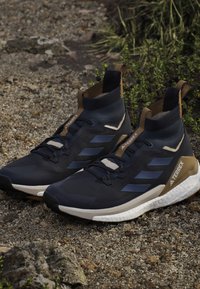 Marineblaue Sportschuhe mit hohem Knöcheldesign, ausgestattet mit einem strukturierten Obermaterial, sandfarbenen Akzenten und einer weißen gepolsterten Sohle, geeignet für Outdoor-Aktivitäten.