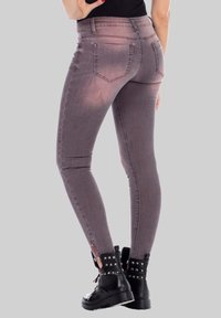 Jean skinny gris à la texture lisse, avec une taille mi-haute, deux poches arrière et des zippers aux chevilles, associés à des bottes de combat noires cloutées.