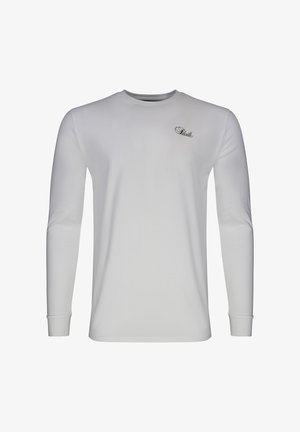 Valge pikkade varrukatega ümmarguse kaelusega särk, mille vasakul rinnal on väike must kursiivkirjas tekstlogo.