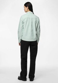 Gestreepte groen-witte blouse met kraag, lange mouwen en een achterplooitje, gecombineerd met zwarte broek en chunky zwarte schoenen.