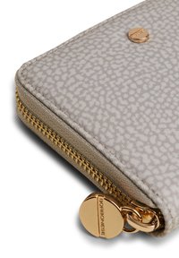 Beige Geldbörse mit einer strukturierten Stoffoberfläche, goldfarbener Reißverschlussbeschläge und einem markierten Metallelement am Reißverschlusszug.