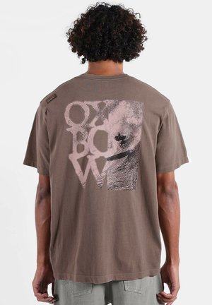 T-shirt en coton marron avec un grand imprimé graphique sur le dos en rose clair, affichant "OXBOW" accompagné d'une illustration de scène de surf.