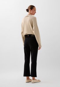 Beige knit sweater with a relaxed fit, black high-waisted jeans, and nude flats. Features a collar and subtle texture.