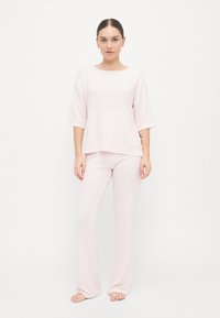 Gaiši rozā mājas apģērba komplekts, kurā ietilpst īsām piedurknēm tops ar apaļu dekoltē un brīvu piegriezumu, kopā ar pieguļošām, taisnām biksēm.