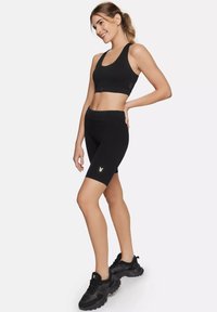 Crni sportski crop top i odgovarajući biciklistički šorts, s glatkom teksturom, prilagođenim dizajnom i malim logotipom u metalik detalju.