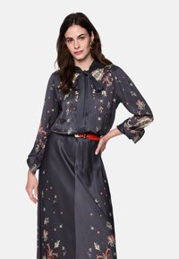 Dunkelgraue Bluse mit Blumenmustern in Rot, Creme und Gold. Verfügt über eine Schleifenbindung am Hals, lange Ärmel und eine glatte Satinstruktur.