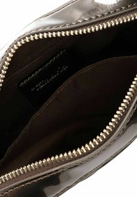 Glänzendes, dunkelbraunes Innenfutter einer Tasche mit einem goldenen Reißverschluss. Eine kleine Innentasche ist sichtbar, mit einem schwarzen Etikett.