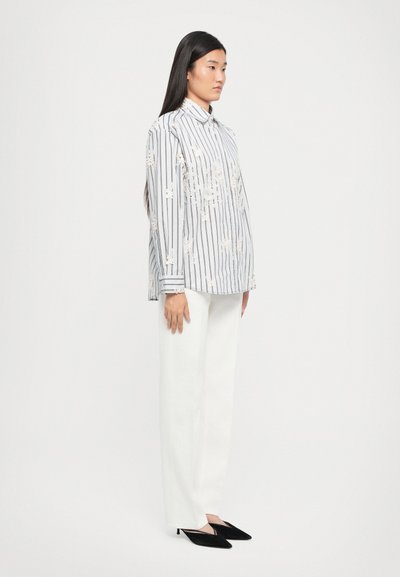 Striped button-up shirt with embroidered floral details, paired with white wide-leg pants and black mules, set against a neutral background.