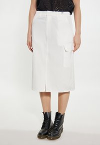 Witte knielange rok met een split aan de voorkant, zijzakken en een relaxte pasvorm. Gemaakt in combinatie met zwarte veterschoenen voor contrast. Gladde textuur.