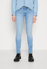Ljusblå slim fit-jeans av denim med en blek tvätt, med bakfickor, dragkedja och som bärs med svarta snörade klumpiga stövlar.