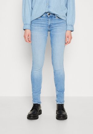Jeans skinny de color azul claro, hechos de denim con un lavado desgastado, que cuentan con bolsillos traseros, cierre de cremallera y se combinan con botas gruesas de encaje negras.
