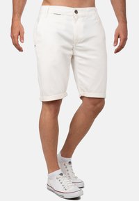 Shorts en denim blanc avec une coupe slim, des ourlets retroussés, une fermeture à bouton à l'avant et des poches latérales. Assortis à des baskets blanches.