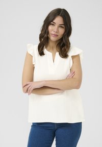 Haut blanc à manches courtes avec des accents de volants et un décolleté en V, fabriqué à partir d'un tissu texturé. Associé à un jean bleu.