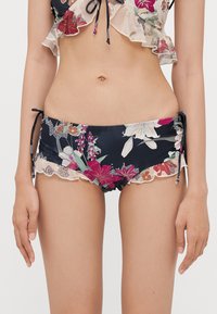 Bikini-set med blomstermønstrete topp med volanger og mørk marinebunn med kontrasterende blonderkant og justerbare bånd.