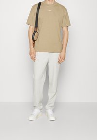 Beige puuvillane t-särk, millel on "HUGO" logo, kombineerituna heledate hallide dressipükstega. Aksessuaarideks on rihmaga crossbody kott ja valged tossud.