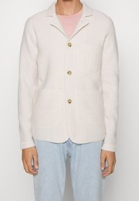 Jasnoróżowa kurtka z mieszanki wełny z wyciętym kołnierzem, zapięciem na guziki z przodu, dwoma naszywanymi kieszeniami i teksturowaną tkaniną. Długie rękawy z mankietami.