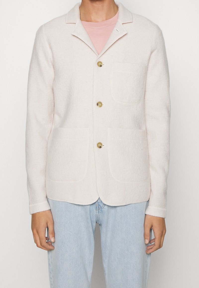 Jasnoróżowa kurtka z mieszanki wełny z wyciętym kołnierzem, zapięciem na guziki z przodu, dwoma naszywanymi kieszeniami i teksturowaną tkaniną. Długie rękawy z mankietami.