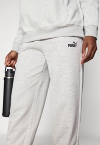 Gray sweatshirt and sweatpants made of soft, textured fabric. Sweatpants feature a black Puma logo. A black water bottle is held in the hand.