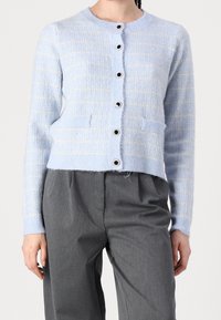 Cardigan bleu clair à motif à carreaux, col rond, fermeture à boutons sur le devant et deux poches avant, fabriqué en tissu tricoté texturé.