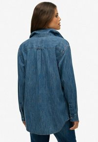 Denim overhemd met lange mouwen in medium blauw, voorzien van een puntkraag, knoopmanchetten en een rugplooitje voor extra bewegingsvrijheid.