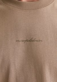 Brązowa bluza z prążkowanym dekoltem, z delikatnym haftem "marcapolodenim" na piersi w dopasowanym, brązowym odcieniu.