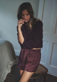 Bordowy sweter dziany zestawiony z satynowymi bordowymi szortami z elastycznym pasem i wiązaniem. Miękka tekstura i luźny krój.