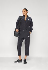 Black zip-up jacket with dark gray accents, matching tapered pants, and black athletic shoes; lightweight material with elasticized waistband.