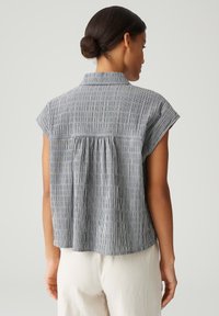 Blusa a maniche corte a righe blu e bianche, con una vestibilità comoda, dettaglio posteriore arricciato e colletto. Tessuto morbido.