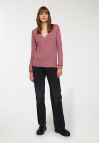 Różowy sweter z dzianiny w serek i prążkowanymi mankietami, zestawiony z czarnymi spodniami typu wide-leg i czarnymi botkami na platformie. Prosty, teksturowany wzór.