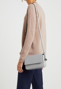 Šedá kožená taška na rameno s hladkým povrchem, klopovým uzávěrem, kontrastním prošíváním a odnímatelným popruhem, vystavená na neutrálním pozadí.