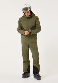 Męska oliwkowa kurtka narciarska i spodnie wykonane z wodoodpornego materiału, z kieszeniami na zamek błyskawiczny, regulowanym kapturem i czarnymi akcentami przy mankietach.
