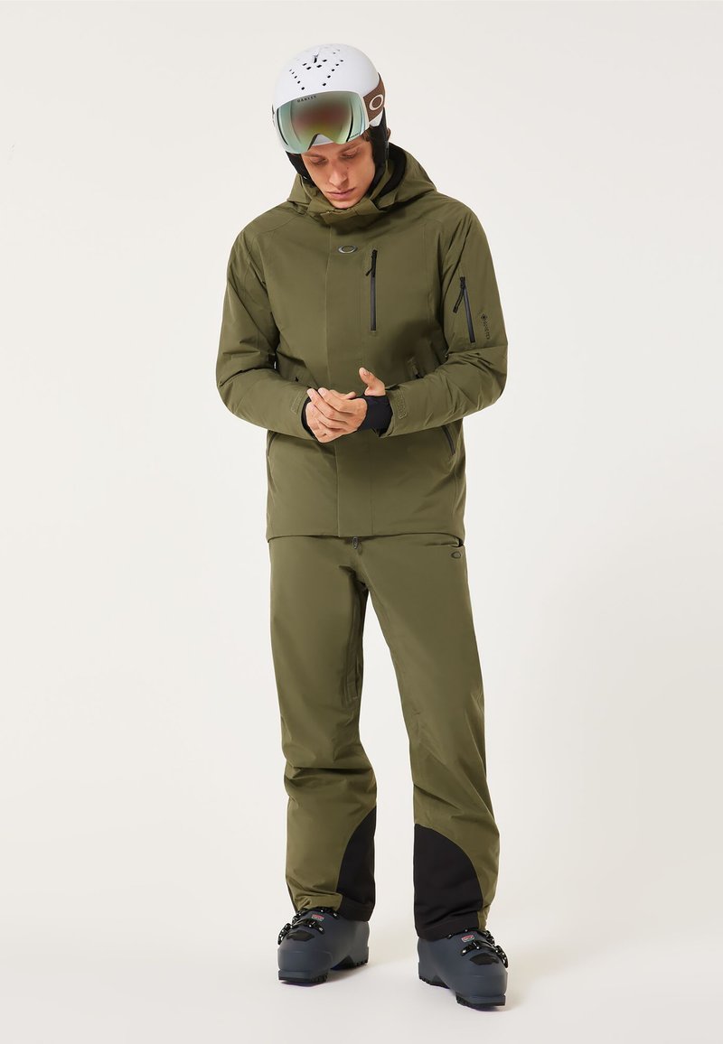 Herren Skijacke und Hose in Olivgrün aus wasserdichtem Material, mit Reißverschlusstaschen, verstellbarer Kapuze und schwarzen Akzenten an den Bündchen.