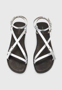 Zilveren leren sandalen met kruiselings gestikte banden, zwarte textuur binnenzool, gespsluiting en platte zool, bieden een minimalistisch ontwerp.