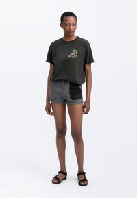 Zwarte katoenen t-shirt met bloemenborduurwerk, gecombineerd met grijze denim shorts met een kleurblokontwerp en rode stiksels. Zwarte sandalen.