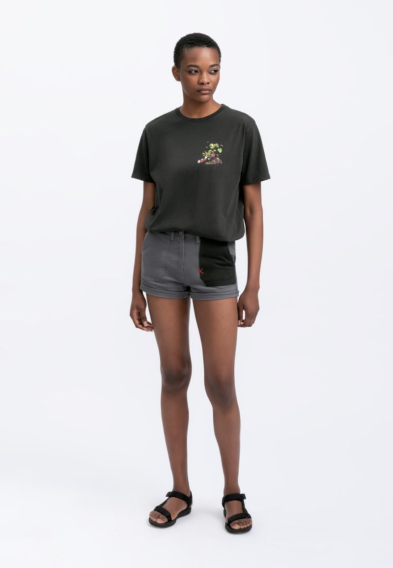 Zwarte katoenen t-shirt met bloemenborduurwerk, gecombineerd met grijze denim shorts met een kleurblokontwerp en rode stiksels. Zwarte sandalen.