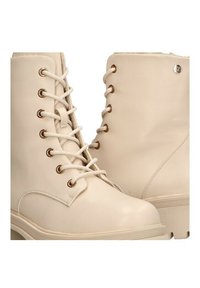 Botines beige hasta el tobillo con un acabado suave y texturizado, que cuentan con ojales en tono dorado, cordones blancos y una suela de goma gruesa.