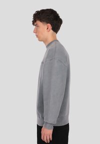 Sivá mikina s okrúhlym výstrihom, rebrovanými manžetami a lemom. Má jemnú textúru a voľný strih, zobrazená z boku.