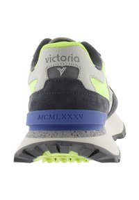 Vista trasera de una zapatilla de ante gris y verde neón con acentos azules, que presenta una suela texturizada y el logotipo de la marca en el talón. La etiqueta "MCMLXXXV" es visible.