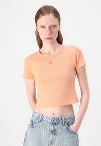 T-shirt à manches courtes, cropped, en coton orange clair avec un col côtelé et un subtil logo brodé "HUGO" sur la poitrine.