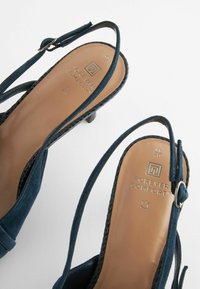 Navy blue suede slingback heels featuring a low heel, an adjustable strap, and a textured insole with "Forever Comfort" branding.