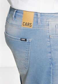 Lichtblauwe denim jeans met een leren label met de tekst "CARS" op de tailleband en een klein geweven label op de zijzak. Contrasterende stikseldetails.