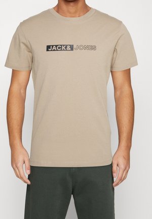 T-shirt en coton beige à manches courtes, arborant un logo rectangulaire noir avec l'inscription "JACK & JONES" sur la poitrine.