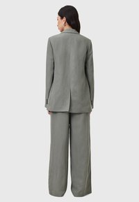 Lichtgrijs pak bestaande uit een op maat gemaakte blazer met een enkele split en wijde broekspijpen, gemaakt van een textiele stof.