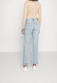 Ljusblå utsvängda jeans med fransade nederkanter och detaljer med patchfickor, tillsammans med en figurnära nude långärmad topp och vita sneakers.