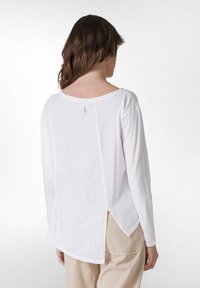 Maglia bianca a maniche lunghe con scollatura rotonda, tessuto a trama e dettaglio posteriore con spacco, abbinata a pantaloni beige.