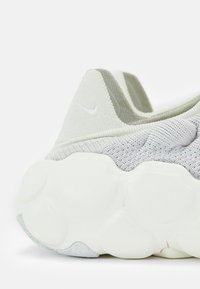 Ljusgrå stickad sneakers med tjock, texturerad vit sula och låg ankla som har en broderad Nike swoosh-logotyp.